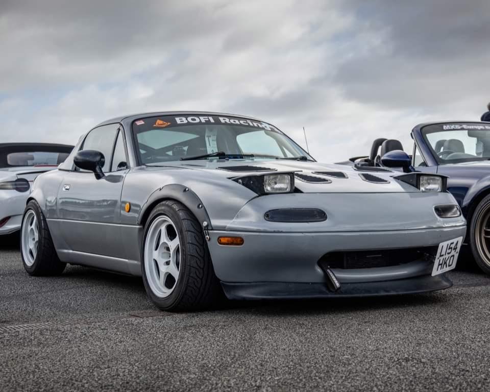 Nardo grey mx-5 parked at Japfest Car show at Silverstone. Mx-5 has wide arches, wide rota slipstream wheels n white colour, big sunstrip with Bofi Racing logo and front splitter.